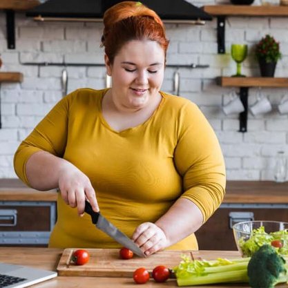 Übergewichtige Frau schneidet Gemüse