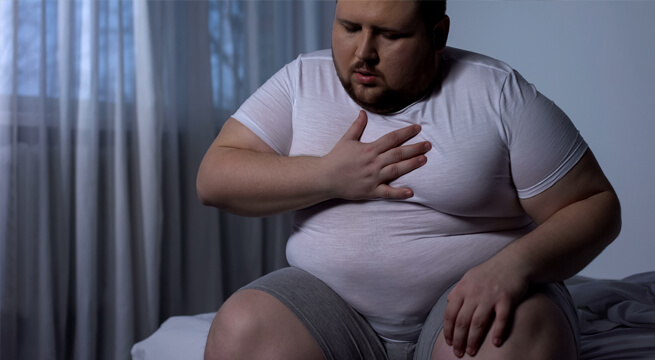 Übergewichtiger Mann sitzt mit Herzproblemen auf der Bettkante