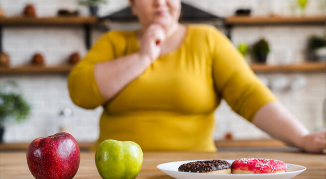 Adipöse Frau entscheidet sich zwischen Apfel oder Donut